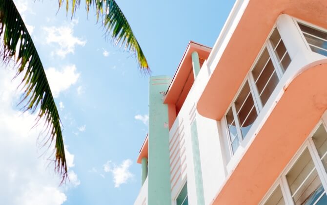 The corner of a beach house and a clear blue sky with palm leaves.